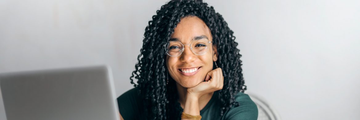 A woman with her laptop open smiles at the camera.
