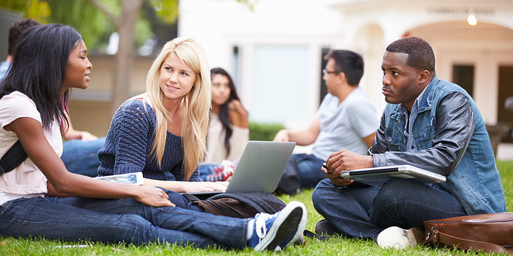 Three students sitting on the grass of a campus quad discussing how education credits help them afford college. 