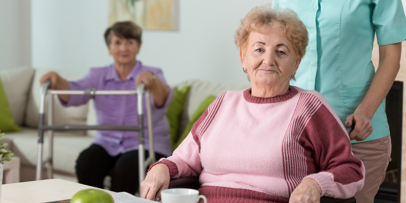 Two seated older women receiving help from a care worker which qualifies for the Child and Dependent Care Credit.