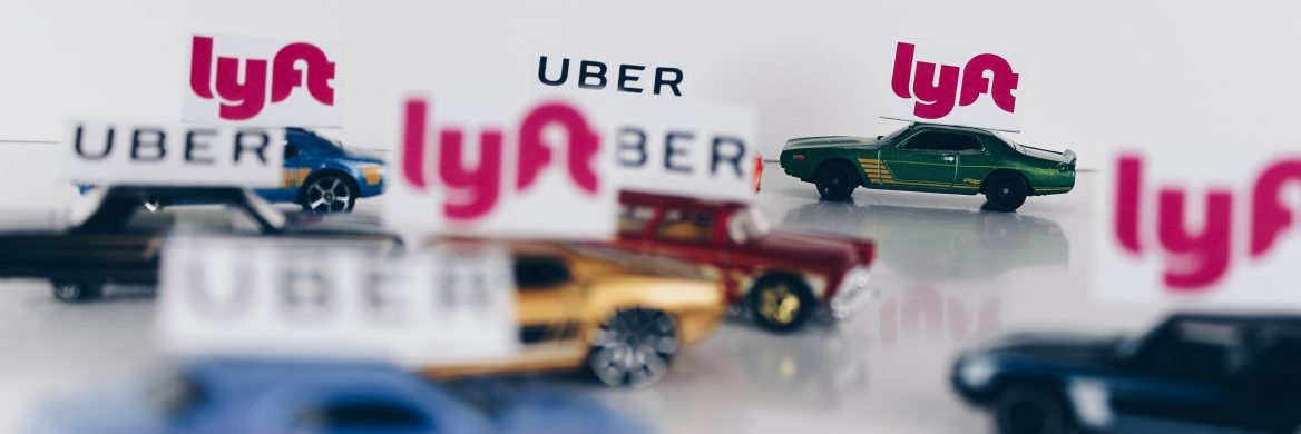 Toy cars that each have a Uber or Lyft sign on the top of them are on a table.