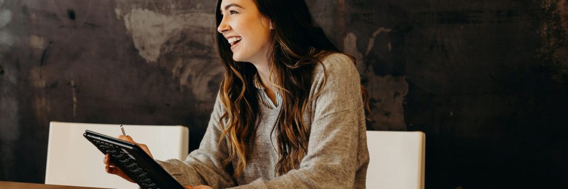 A woman smiles while holding a tablet.