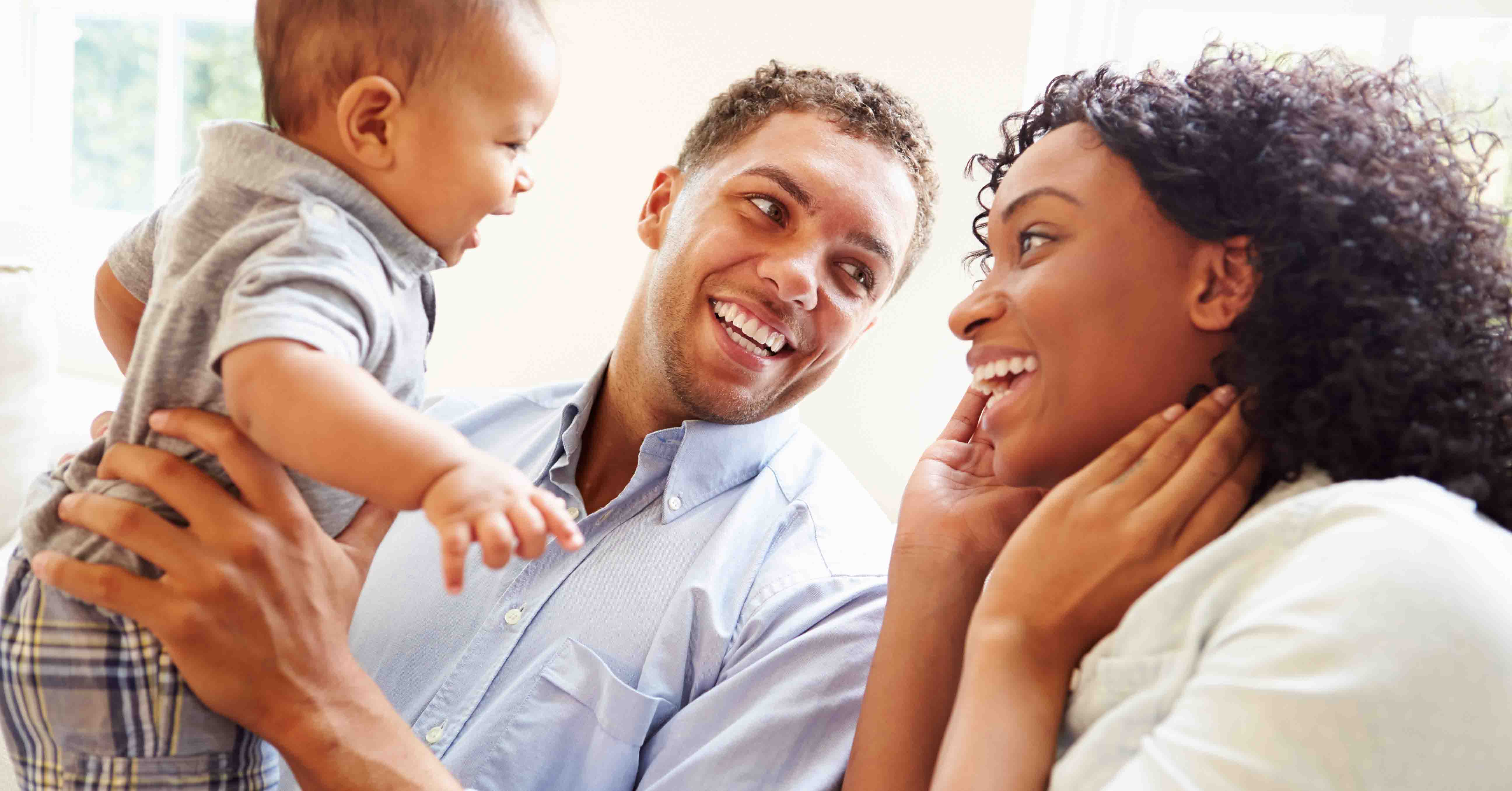 “A father is smiling about being eligible for the Child Tax Credit as he holds his baby up to look at his happy mother.