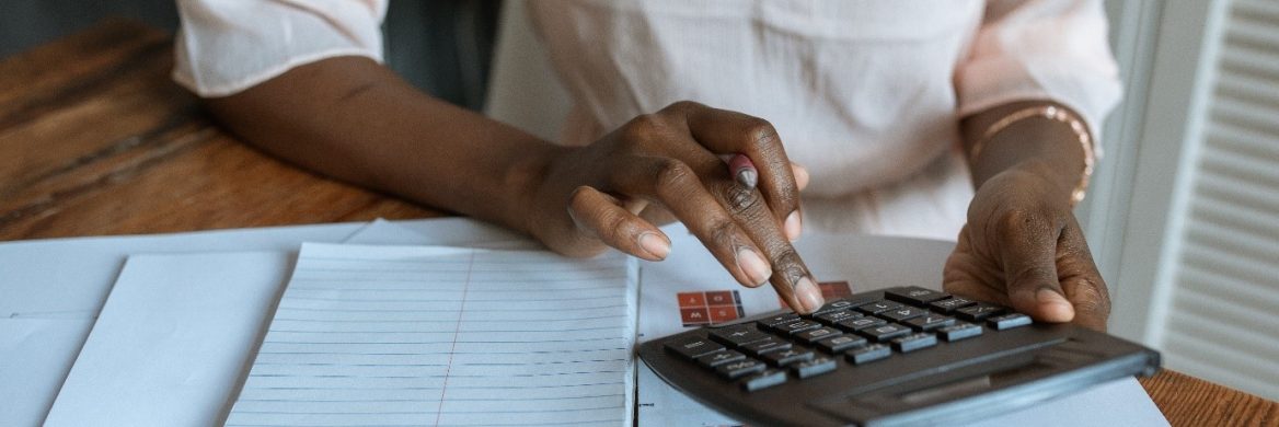 someone sitting at a table with a notebook, typing on a calculator. The person's head is cropped.