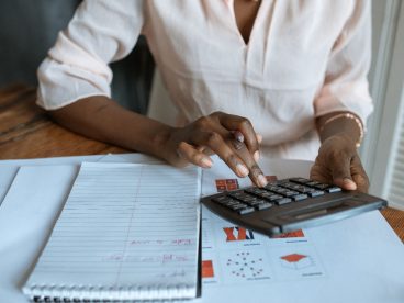 someone sitting at a table with a notebook, typing on a calculator. The person's head is cropped.