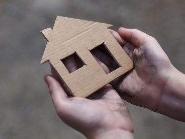 Hands holding a cardboard cutout of a house.