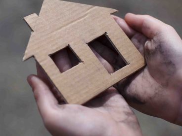 Hands holding a cardboard cutout of a house.