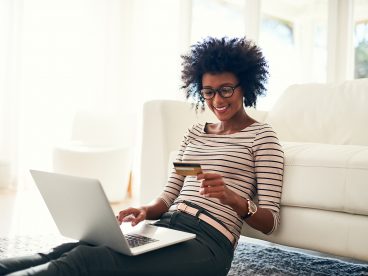 A woman smiles while looking at a debit card with her laptop open.