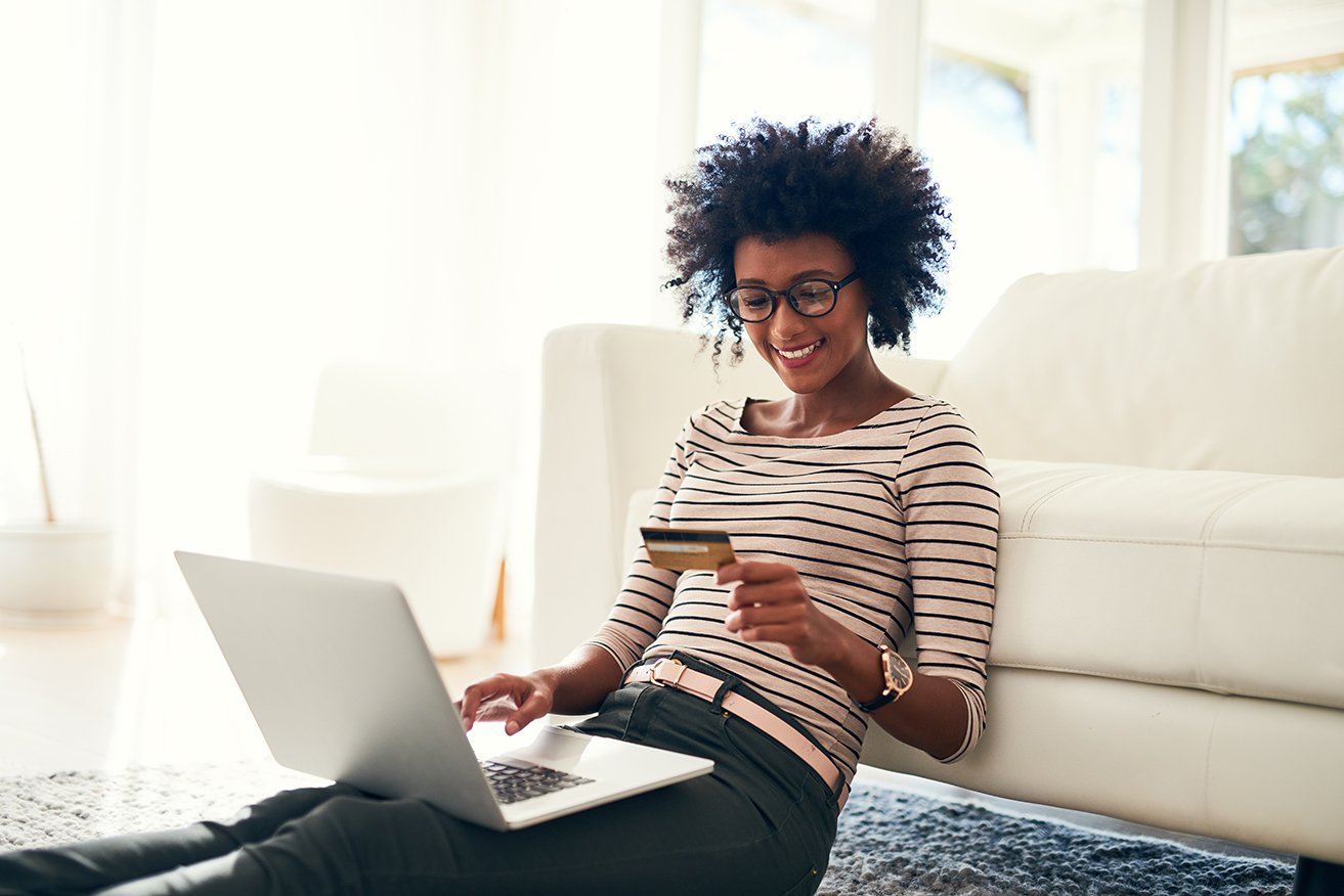 A woman smiles while looking at a debit card with her laptop open.