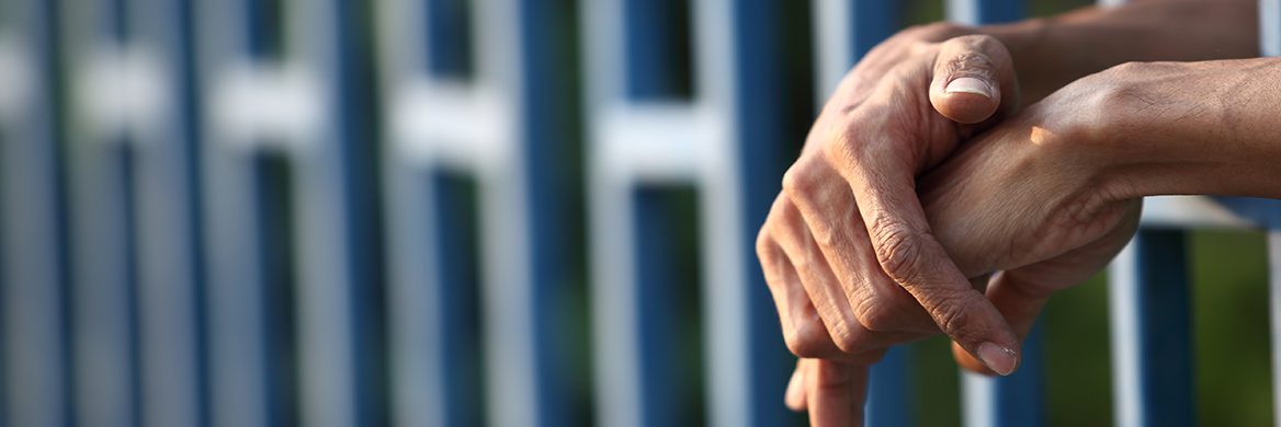 Hands resting between jail bars.
