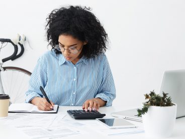 Woman writes in a notebook while using a calculator.