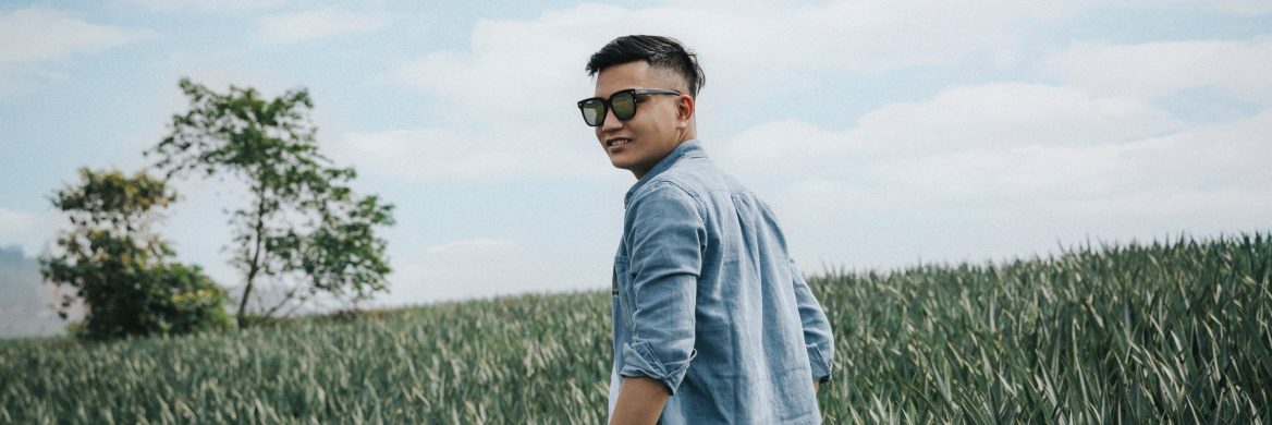 Person with sunglasses on standing in a field looking over their shoulder toward the camera.