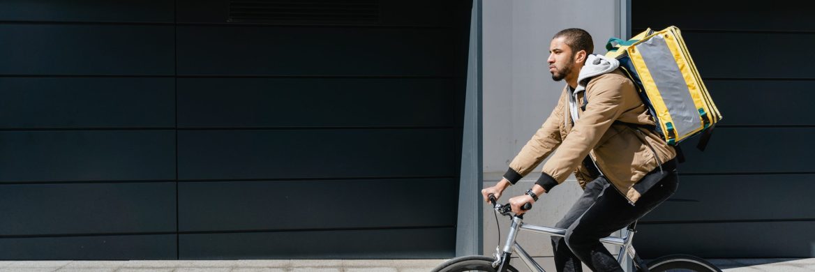 A man with a food delivery backpack riding a bike.