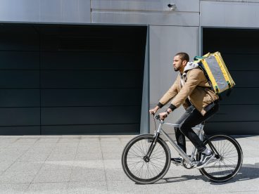 A man with a food delivery backpack riding a bike.