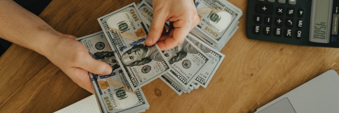 Hands counting stacks of one-hundred-dollar bills on a table with a calculator displaying 4,500.