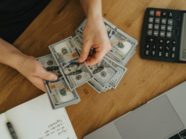 Hands counting stacks of one-hundred-dollar bills on a table with a calculator displaying 4,500.