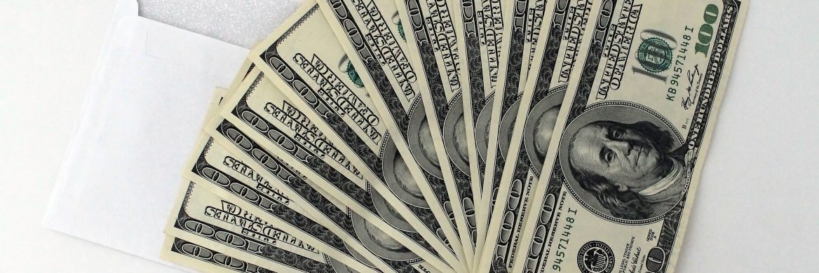 Twelve one-hundred-dollar bills fanned out on top of an envelope – the amount a family of two received from the second stimulus checks.