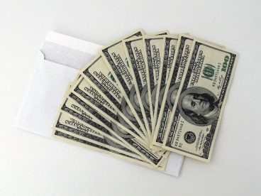 Twelve one-hundred-dollar bills fanned out on top of an envelope – the amount a family of two received from the second stimulus checks.