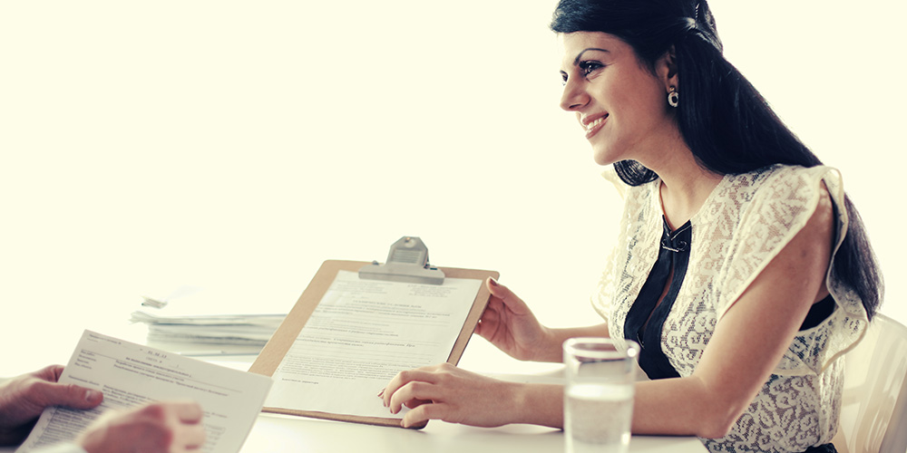 A counselor smiles while holding a clipboard and discussing financial information with a client. 
