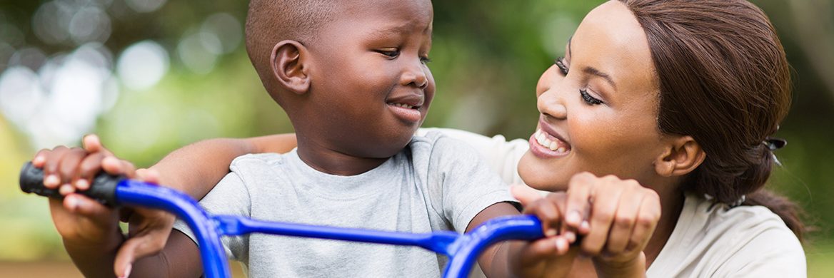 A mother assists her child to ride a bike.