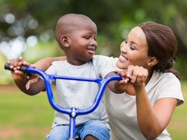 A mother assists her child to ride a bike.
