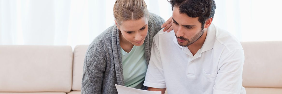 A worried man and woman sitting on a couch reading a notice from the IRS.