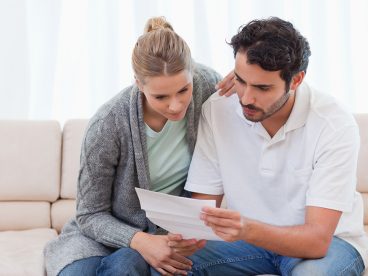 A worried man and woman sitting on a couch reading a notice from the IRS.