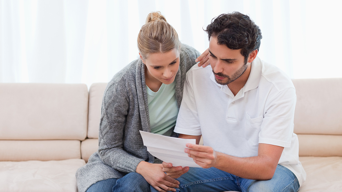A worried man and woman sitting on a couch reading a notice from the IRS.