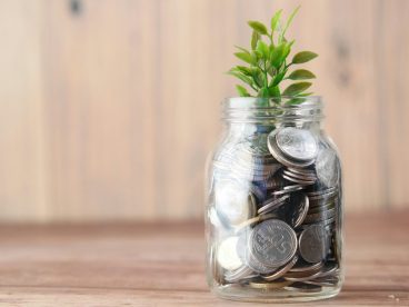 Coins fill a clear glass jar and a plant sprouts from the top.